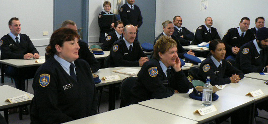 A group of correctional officers sitting at desks and standing next to wall