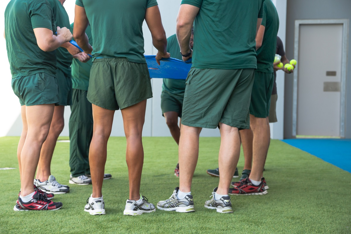 Eight male inmates dressed in green, standing in a circle, some holding tennis balls 