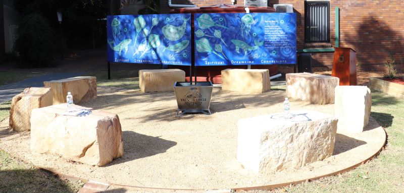 Sandstone blocks in a circle around a firepit, Aboriginal mural in background