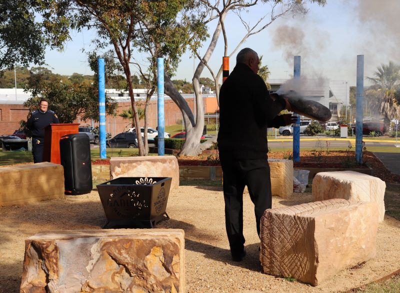 Man holding coolamon with smoking leaves in the yarning circle