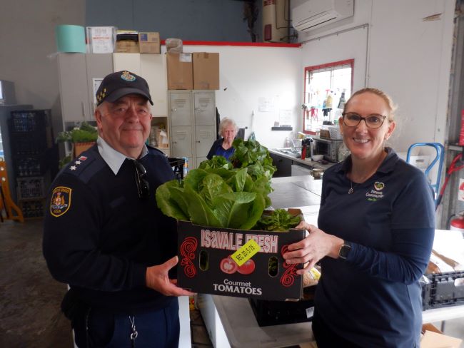 Peter hands a box of vegetables to Kat inside the shop 